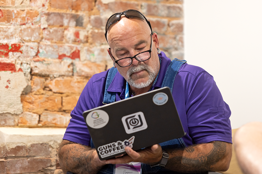 A man holds a laptop computer as he works on a presentation while sitting on a bench inside a building.