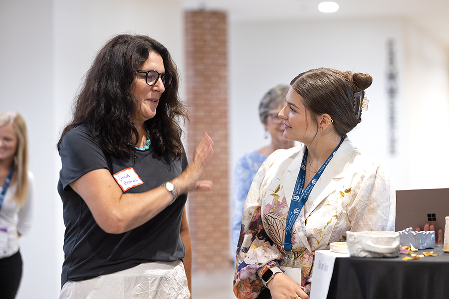 Two women talk in a hallway. One woman is asking the younger one questions about a project she is presenting on.