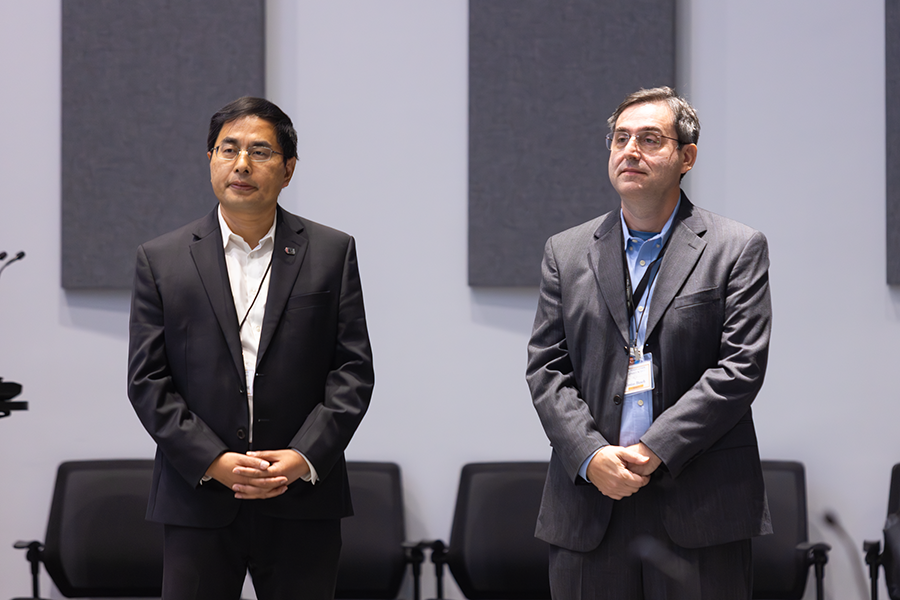 Two men stand side by side as they listen to a speaker during a lecture.