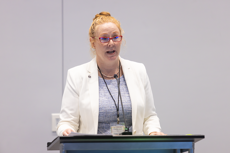 A woman stands at a podium and speaks to a large group of people.