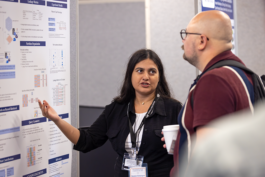 A college woman speaks with a man and talks about her scientific poster. She is pointing to one section of the poster.