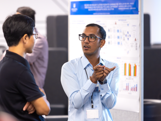 Two college men talk during a poster session for a symposium. One man is using his hands to indicate what he is describing.