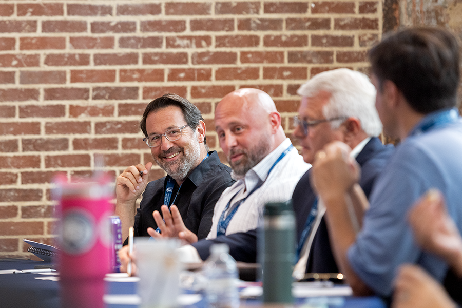 A man looks down a crowded table at another person and smiles.