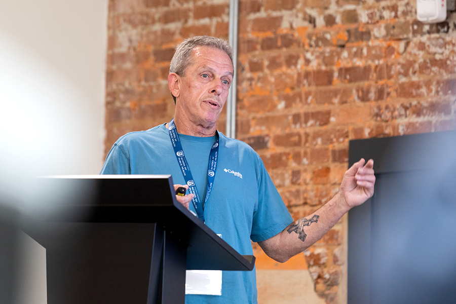 A man stands at a podium and gives a presentation to a large group of people gathered in a conference room.