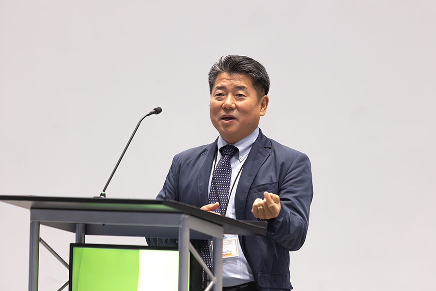 A man stands at a podium with a microphone while speaking to a large group of people gathered in an auditorium.