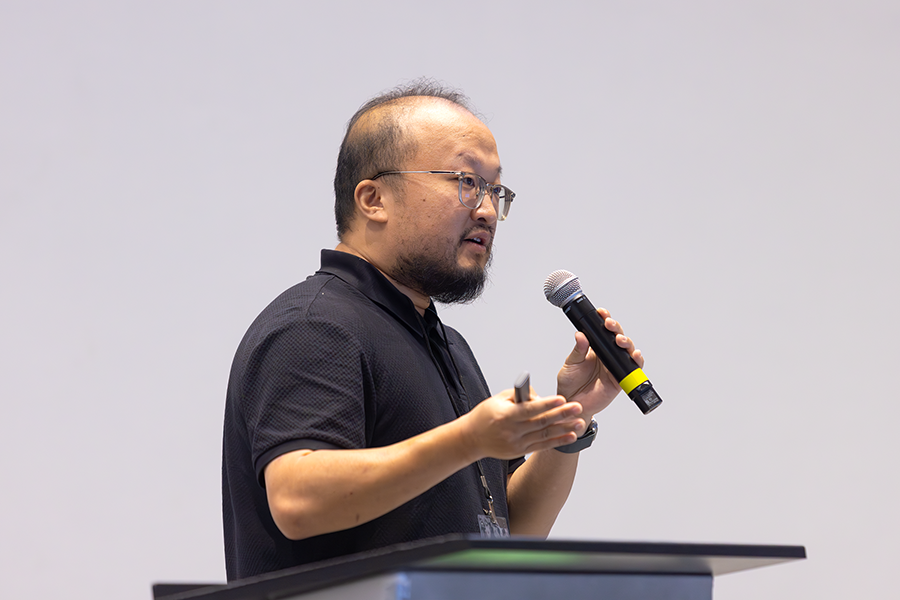 A man stands at a podium with a microphone while speaking to a large group of people gathered in an auditorium.