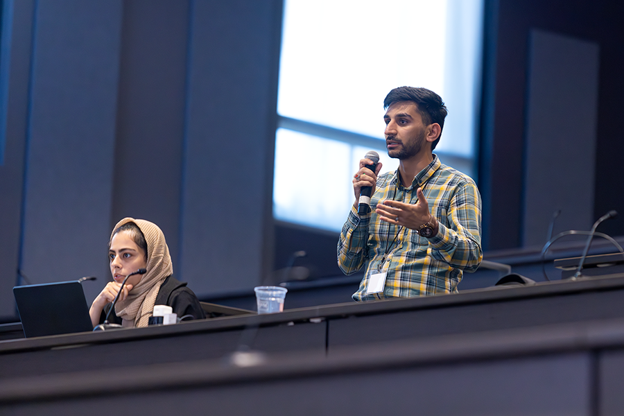 A college man stands up in the audience of a large auditorium and asks a question of a speaker during a presentation.