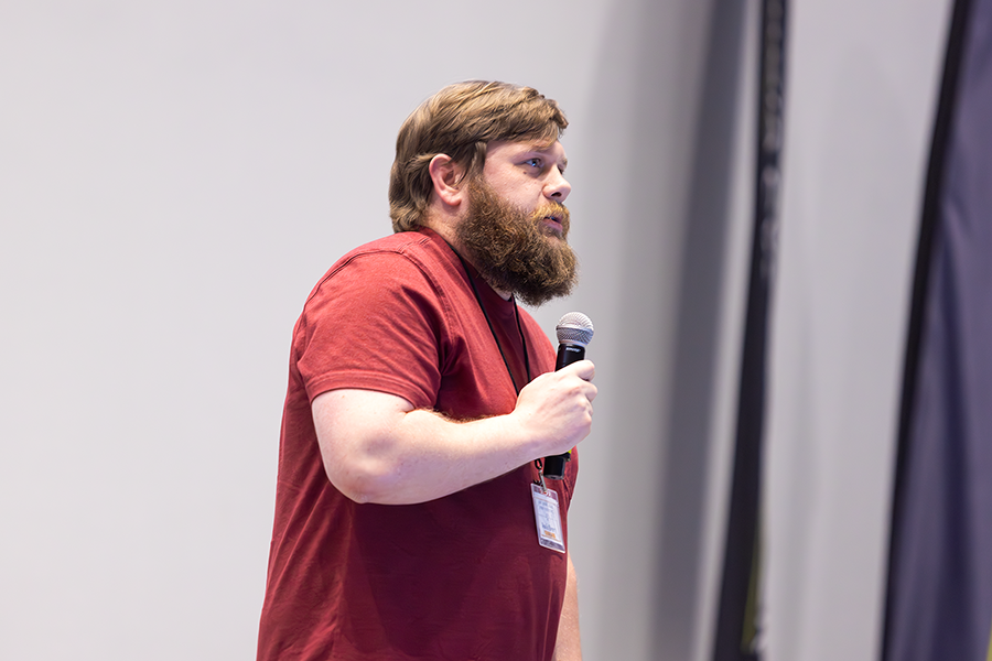 A man stands at a podium with a microphone while speaking to a large group of people gathered in an auditorium.