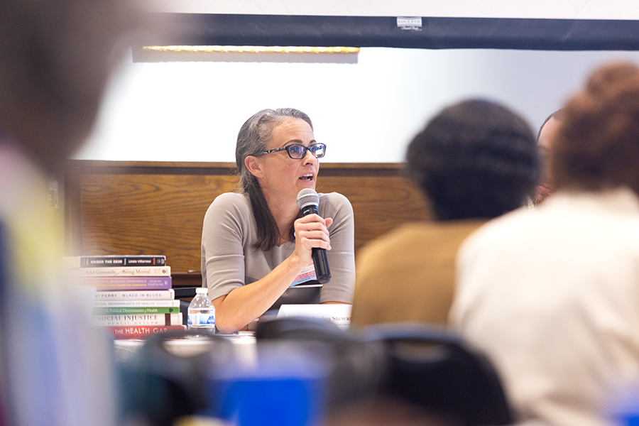 A woman holds a microphone while speaking to a large group of people.