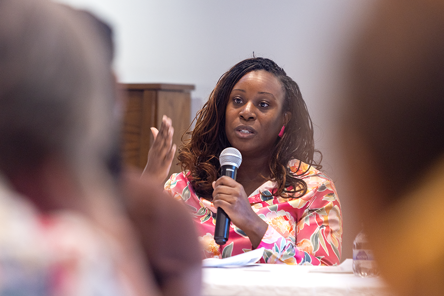 A woman holds a microphone while speaking to a large group of people.