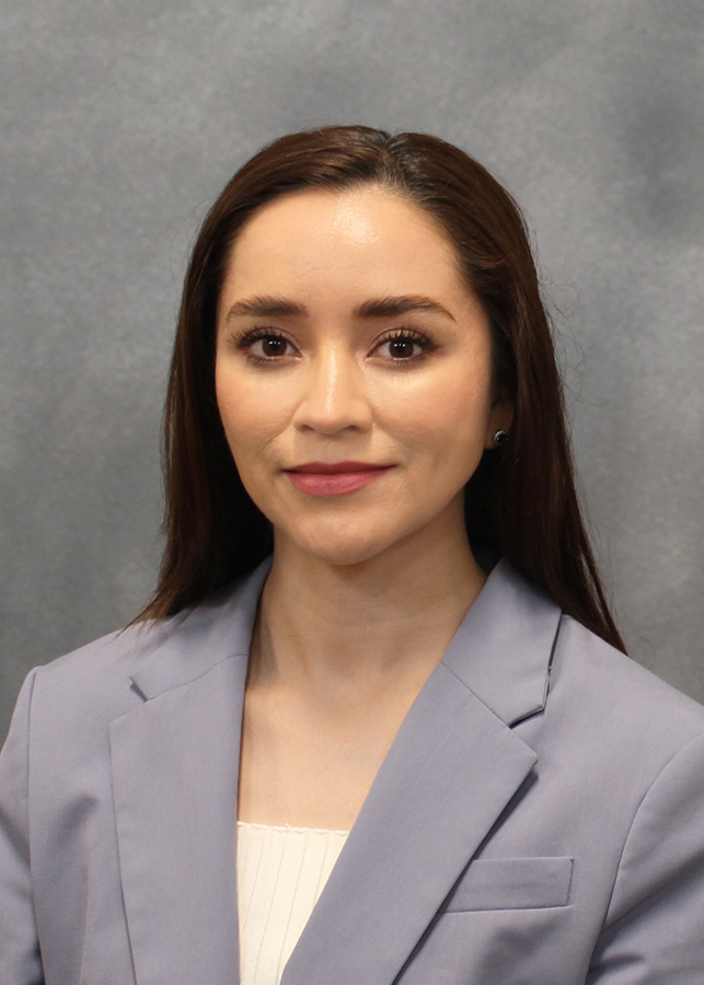 A woman in a bluish-gray suit smiles at the camera