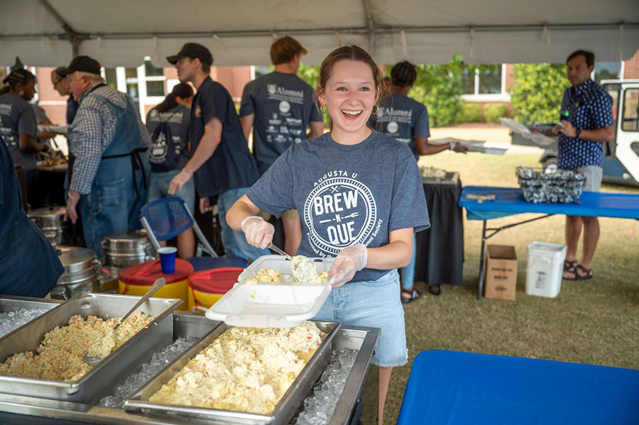 A woman scoops out potato salad into a to-go box.