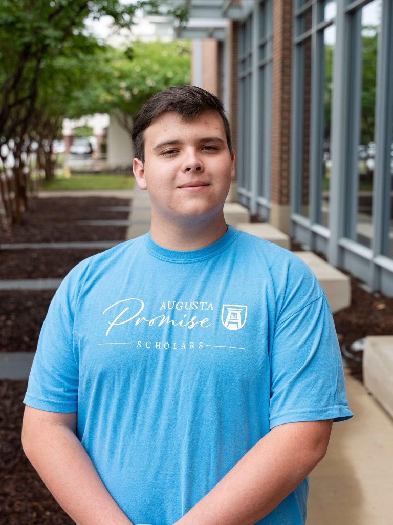 A college-aged male student poses for a photo outside of a building.