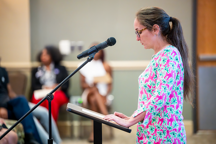 A woman stands in front of a large crowd at a microphone and reads part of the U.S. Constitution.