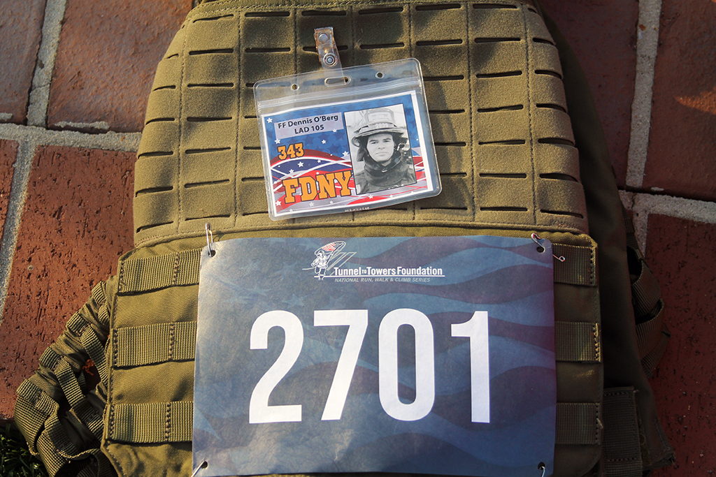 A backpack lays on the ground with a racing number 2701 and photo ID card from a New York firefighter
