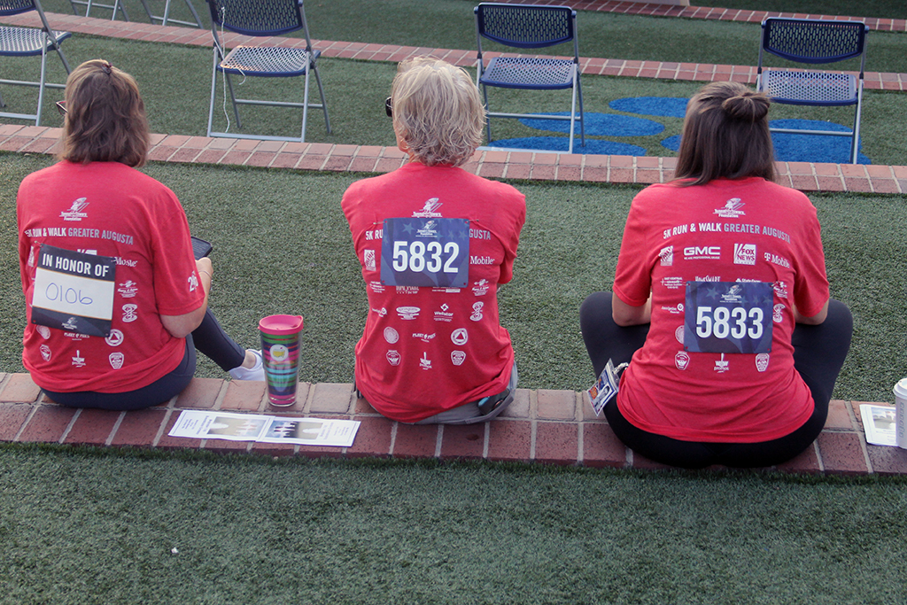 Three women with racing numbers on their back wear red 5K Run & Walk Greater Augusta t-shirts