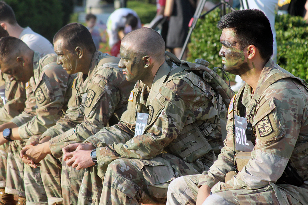 Men in military uniforms and camo face paint sit on a ledge
