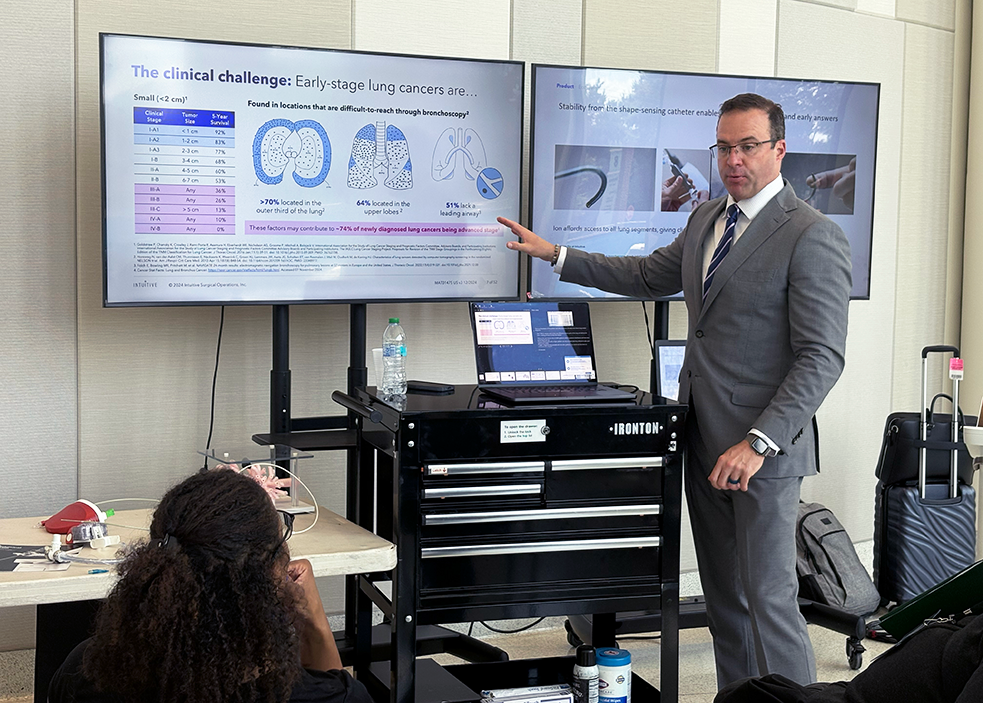 A man in a suit points at a screen with a presentation about early-stage lung cancer on it.