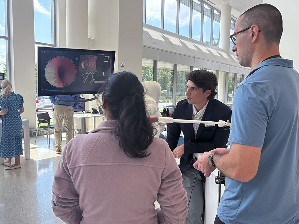 Two male and one female medical fellows observe a screen showing the inside of a trachea.