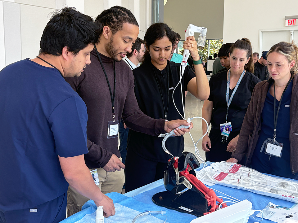 A group of three female and two male pulmonologists gather around a table and practice pulmonology techniques.