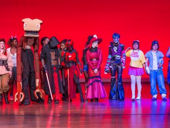 College-aged students lined up on a stage dressed in costumes.