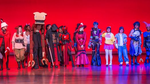College-aged students lined up on a stage dressed in costumes.