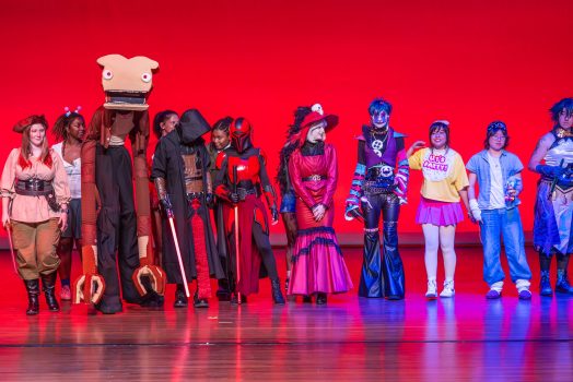 College-aged students lined up on a stage dressed in costumes.