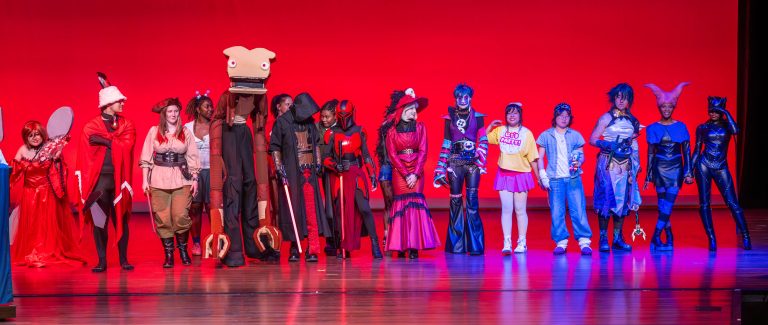 College-aged students lined up on a stage dressed in costumes.