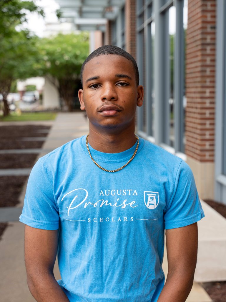 A college-aged male student poses for a photo outside of a building.