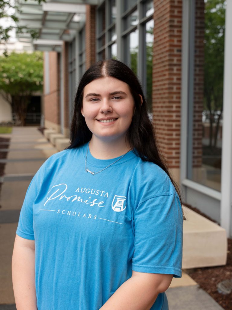 A college-aged female student poses for a photo outside a building.