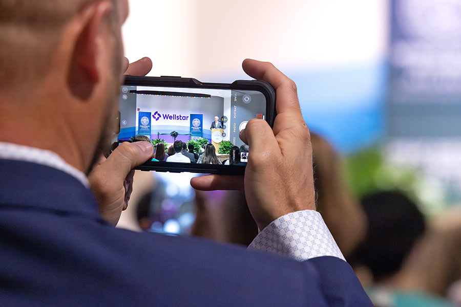 A man takes a photo of a speaker at a podium with his cellphone .
