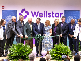 A group of 10 people take part in a ceremonial ribbon cutting ceremony on a stage in front of a larger group of people.