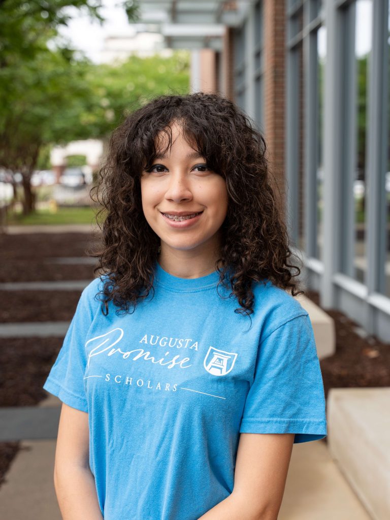 A college-aged female student poses for a photo outside a building.