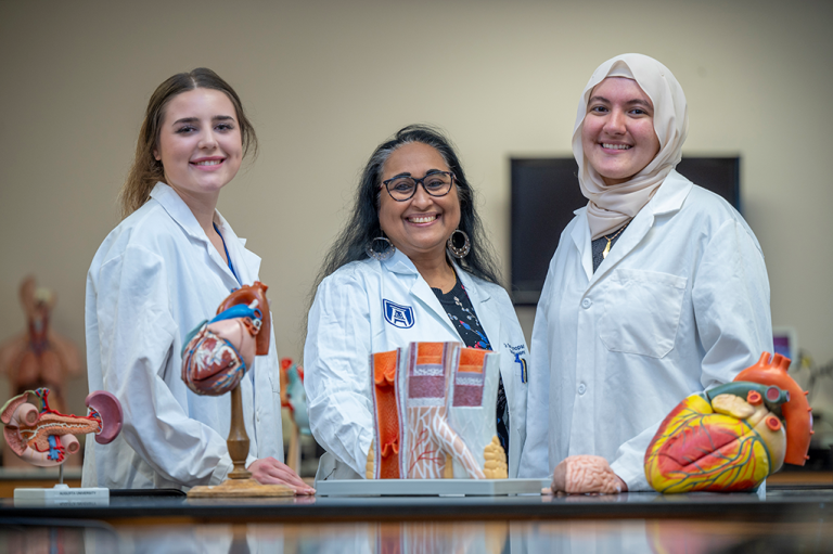 Three women in white coats pose with medical models.