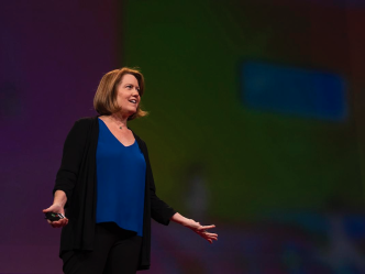 A woman presents on stage to a large group of people.