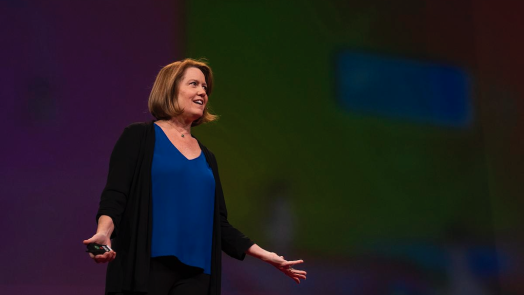 A woman presents on stage to a large group of people.