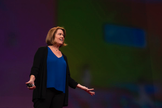 A woman presents on stage to a large group of people.