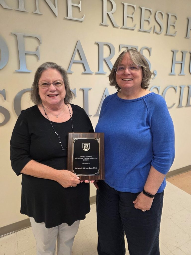 Two women standing in a hallway holding a plaque.