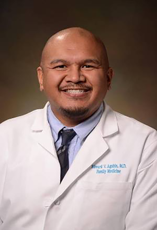 A man wearing a lab coat smiles at the camera.