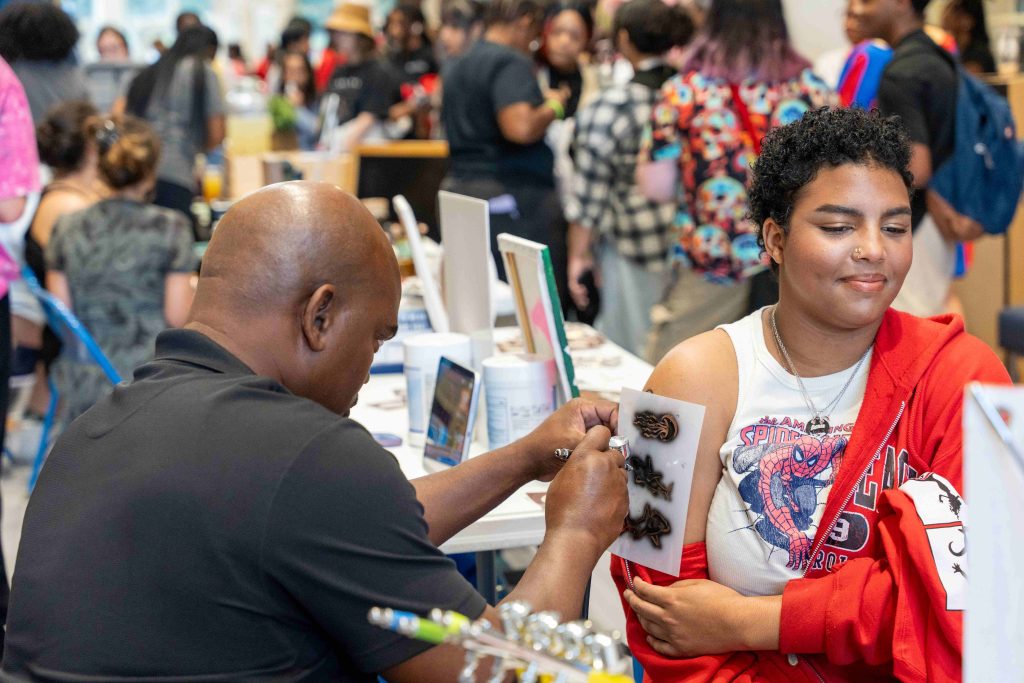 A man airbrushes a temporary tattoo onto a girl's arm.