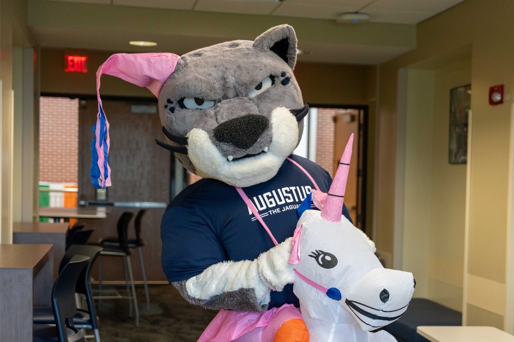 A college mascot shaped like a large cat is dressed in a unicorn cosplay costume.