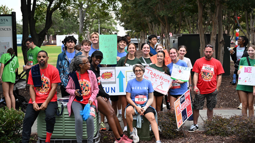 A large group of people hold signs and cheer as cyclists ride by during a race.
