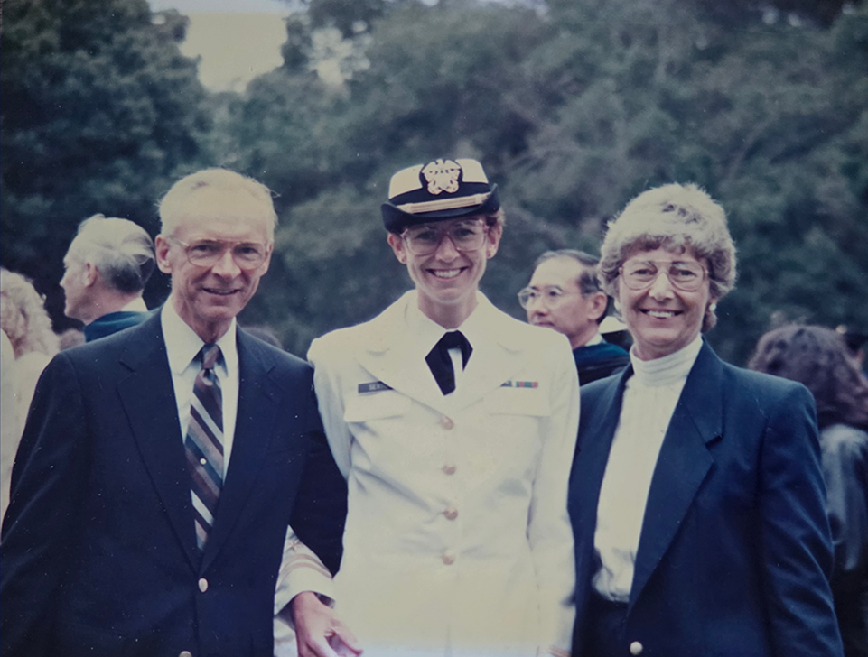 A woman wearing a U.S. Navy uniform poses with her parents at a graduation ceremony for a master's program at the U.S. Naval War College.