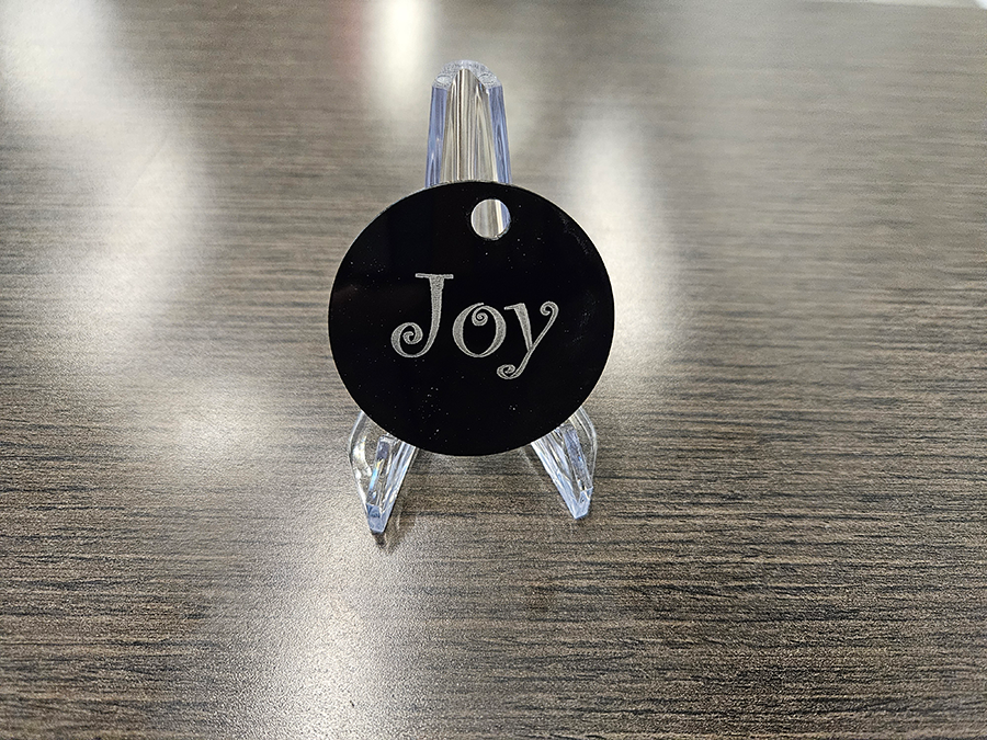 A circular holiday ornament. The word "Joy" is printed on it.