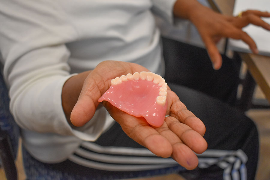 A person's hand holding a 3D-printed model of the top of a human mouth with teeth.
