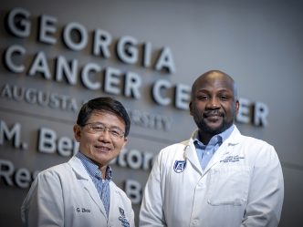 Two men in lab coats in front of Georgia Cancer Center sign