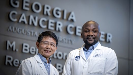 Two men in lab coats in front of Georgia Cancer Center sign