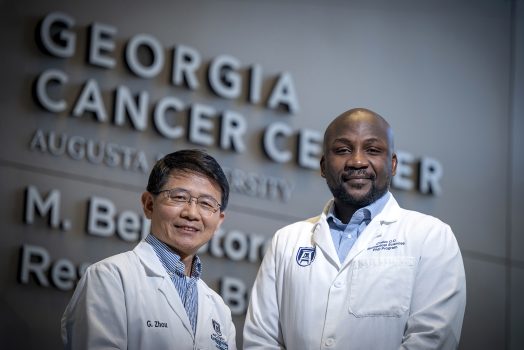 Two men in lab coats in front of Georgia Cancer Center sign
