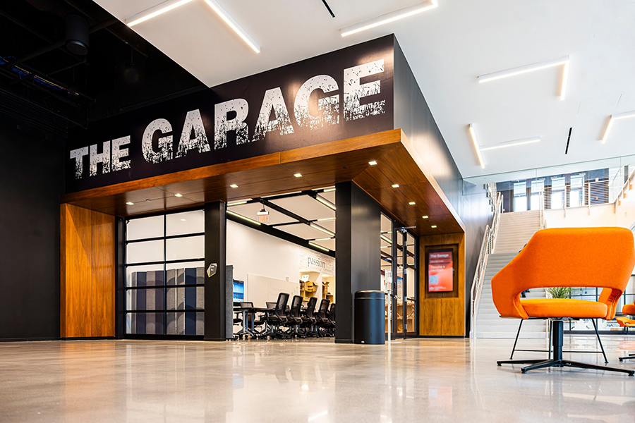 An open space inside a large building. There is a large sign over a garage-style door that reads "The Garage."