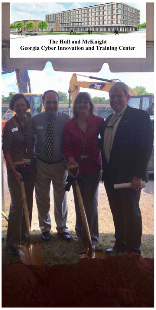 Two women and two men pose for a photo during a groundbreaking ceremony for a new modern building on a college campus.